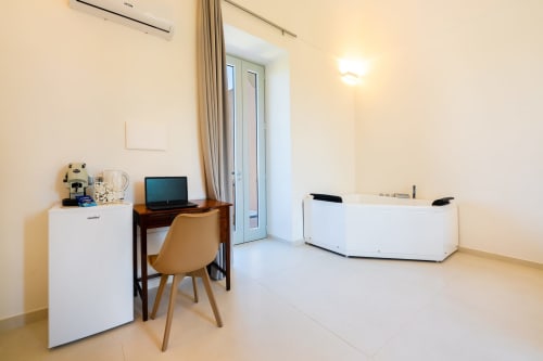 Camera moderna negli Origenes Rooms di Procida con scrivania, TV, mobili bianchi e accesso a balcone con vista mare