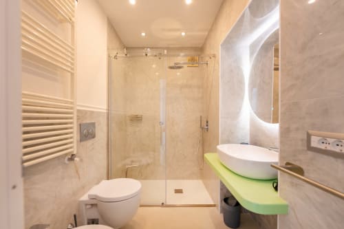 Bagno moderno presso Origenes Rooms a Procida con piastrelle in marmo, doccia in vetro, wc bianco e ripiano del lavabo verde