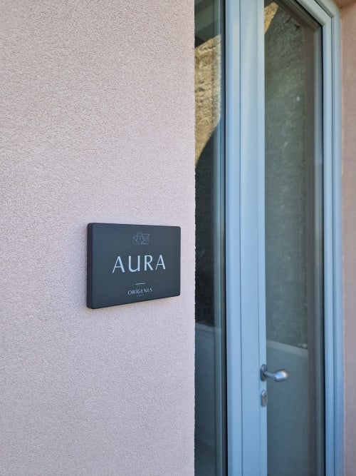 Targhetta della camera Aura presso Origenes Rooms, appartamento con vista mare a Procida, montata su parete rosa testurizzata accanto a vetro
