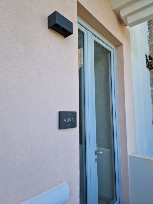 Ingresso della suite Aura presso Origenes Rooms a Procida con porta scura, targhetta e applique murale