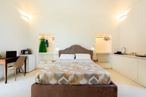 Camera luminosa presso Origenes Rooms a Procida con letto imbottito marrone, scrivania, angolo cottura e vista mare dal balcone