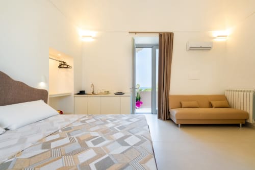 Camera da letto moderna con vista sul mare presso Origenes Rooms, Procida. Letto, divano, angolo cottura e porta-finestra sulla terrazza.