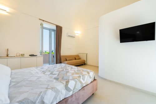 Camera moderna a Origenes Rooms a Procida con vista sul mare, TV, angolo cottura, divano arancione e pavimento in marmo