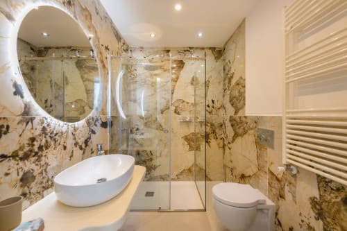 Lussuoso bagno nell'appartamento Aura di Origenes Rooms, Procida con rivestimenti in marmo, lavabo moderno, specchio illuminato e doccia a pioggia