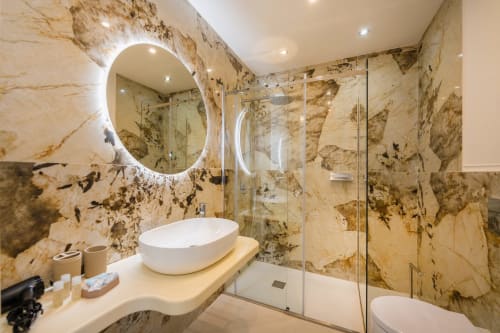 Bagno in marmo di lusso presso Origenes Rooms a Procida, con specchio illuminato, lavabo da appoggio, cabina doccia e finiture dorate
