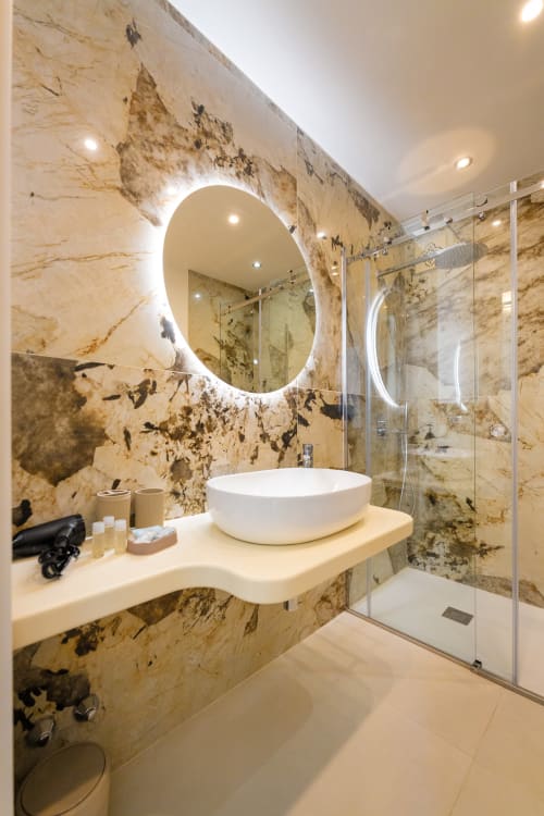 Bagno di lusso nell'appartamento Aura di Origenes Rooms, Procida con pareti in marmo, specchio con illuminazione LED, lavabo bianco e doccia