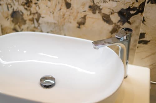 Lavabo in ceramica bianca moderna con rubinetto cromato nel bagno dell'appartamento Aura presso Origenes Rooms, Procida