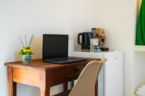 Scrivania in legno con laptop, pianta e caffettiera nell'appartamento Aura di Origenes Rooms, Procida