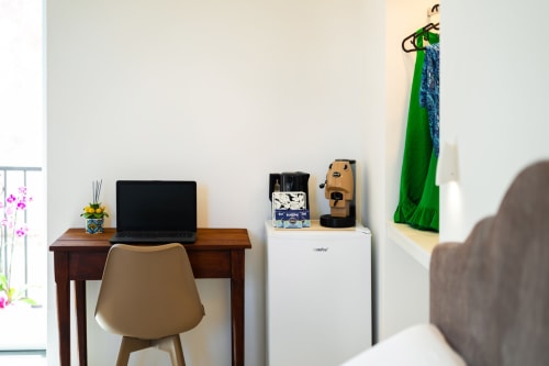 Spazio di lavoro Aura presso Origenes Rooms a Procida con scrivania in legno, computer, macchinetta per caffè e amaca con vista sul mare verde