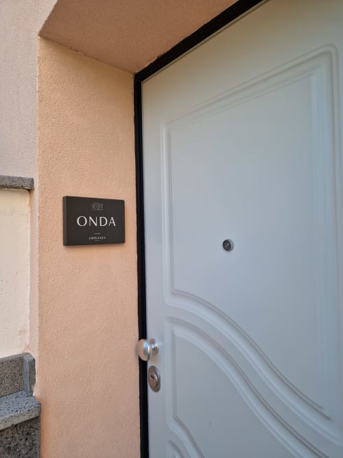 Ingresso della camera Onda presso Origenes Rooms, Procida, con porta nera e dettagli in bianco su parete in intonaco color pesca