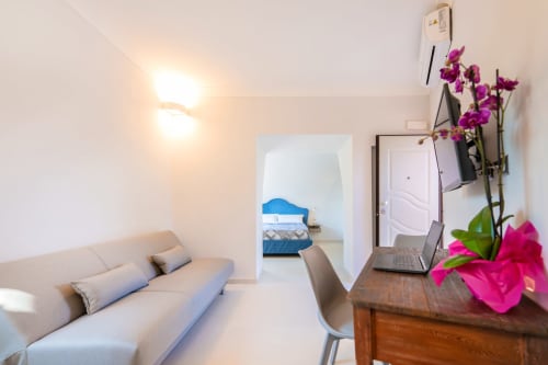 Appartamento Onda presso Origenes Rooms, Procida: elegante living con divano, scrivania, orchidee e vista della camera da letto