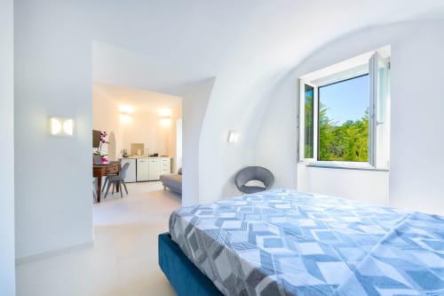 Camera luminosa di Origenes Rooms, Procida con biancheria blu decorata, arredi moderni e vista sul giardino dalla finestra
