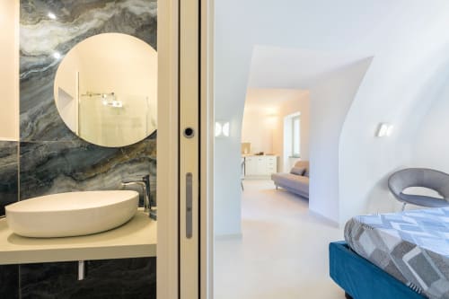 Bagno moderno con pareti in marmo e specchio rotondo nell'appartamento Onda presso Origenes Rooms, Procida