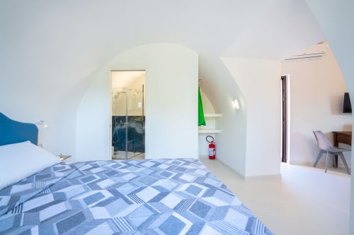 Camera moderna nell'appartamento Onda di Origenes Rooms, Procida, con biancheria blu decorata, muri bianchi voltati, e