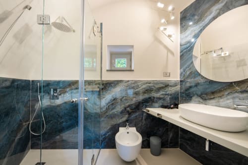 Bagno moderno nell'appartamento Onda di Origenes Rooms, Procida, con piastrelle in marmo blu, lavabo a bacinella, bidet e doccia walk-in.