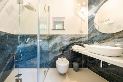 Bagno moderno con pareti in marmo blu, doccia a pioggia, doppi lavabi a bacinella e bidet presso Origenes Rooms, Procida