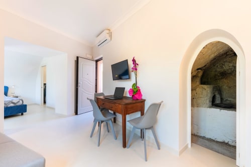 Spazio di lavoro moderno in appartamento Origenes Rooms a Procida con scrivania in legno, sedie grigie, TV e nicchia in pietra ad arco