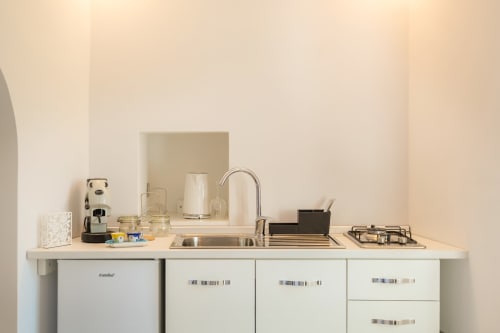 Angolo cottura minimalista nell'appartamento Onda di Origenes Rooms, Procida, con mobili bianchi, fornello a gas e caffettiera