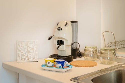 Bancone cucina nell'appartamento Onda di Origenes Rooms, Procida con macchina espresso, tazze da caffè, vasetti e sottobicchieri in sughero