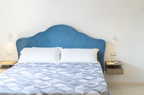 Camera moderna alle Origenes Rooms di Procida con testata imbottita blu, cuscini bianchi, biancheria fantasia e comodino