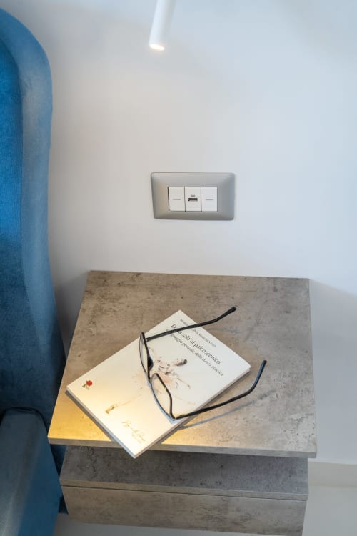 Libri e occhiali da lettura sul comodino in cemento in camera d'albergo moderna a Procida con presa di corrente