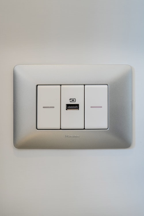 Presa elettrica argentata con porta USB e due interruttori nell'appartamento Origenes Rooms, Procida