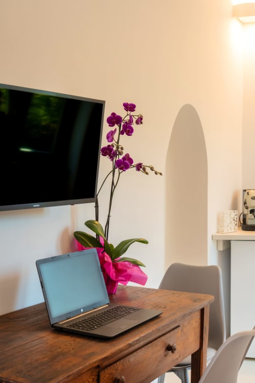 Spazio di lavoro moderno presso Origenes Rooms Procida con laptop, orchidea viola, TV e vista sul paesaggio nell'appartamento Onda