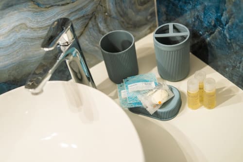 Vanity del bagno presso Origenes Rooms Procida con amenities, contenitori cilindrici grigi, articoli da toeletta e lavabo in marmo