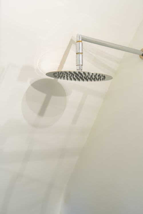 Soffione moderno con finitura metallica montato su parete bianca nel bagno di Origenes Rooms, Procida