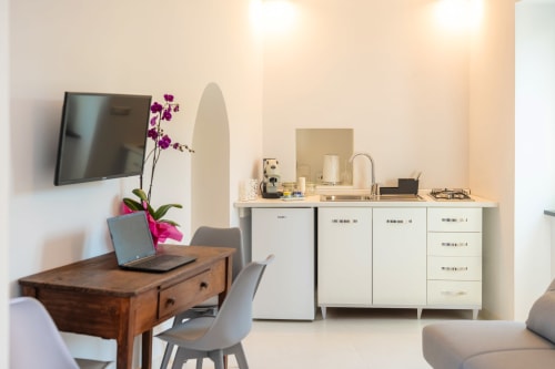Moderno monolocale a Procida con scrivania in legno, laptop, orchidea viola, TV a parete, angolo cottura e design contemporaneo