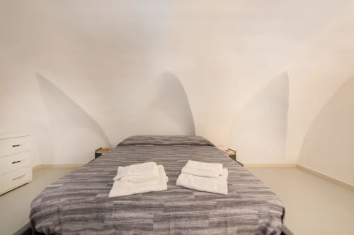 Letto a righe grigie con asciugamani bianchi nell'appartamento Era di Origenes Rooms a Procida, con soffitto bianco a volta