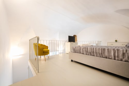 Camera moderna presso Origenes Rooms a Procida con poltrona gialla, letto a righe e vista sui monumenti