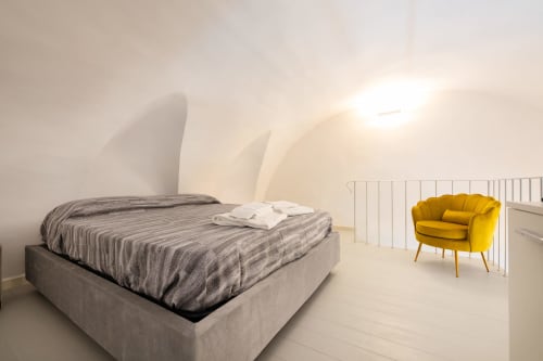 Camera moderna nell'appartamento Era di Origenes Rooms, Procida con letto grigio, poltrona gialla e arredamento bianco minimalista