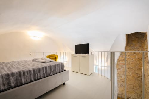Camera da letto moderna in Origenes Rooms, Procida con letto, TV, poltrona gialla e vista sul paesaggio dalla mezzanine