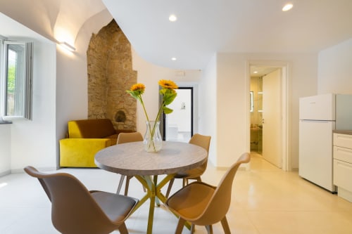 Zona pranzo moderna dell'appartamento Era presso Origenes Rooms, Procida con tavolo rotondo, sedie gialle e volta in pietra