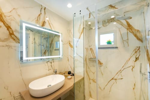 Bagno moderno con pareti in marmo, lavabo a bacinella e doccia con box in vetro presso Origenes Rooms, Procida