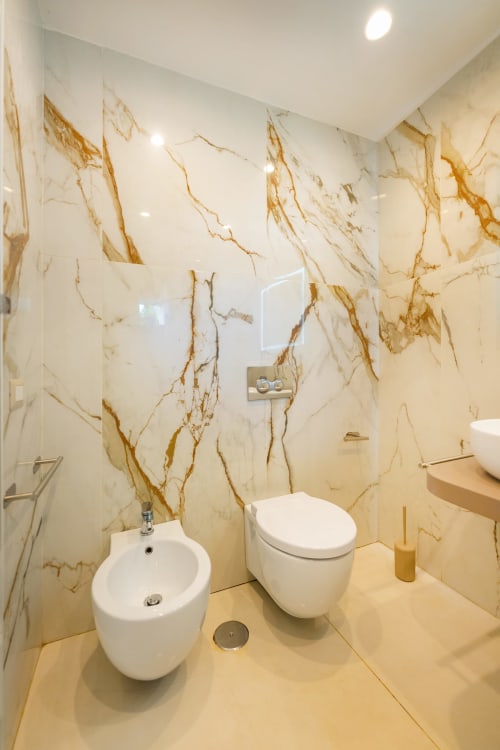 Bagno moderno presso Origenes Rooms, Procida con pareti in marmo color crema, bidet e wc bianchi, riscaldamento a pavimento e incassi
