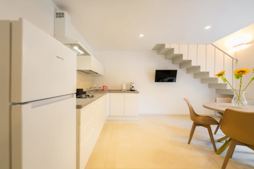 Cucina e zona pranzo moderna a Procida con mobili bianchi, scala e fiori freschi