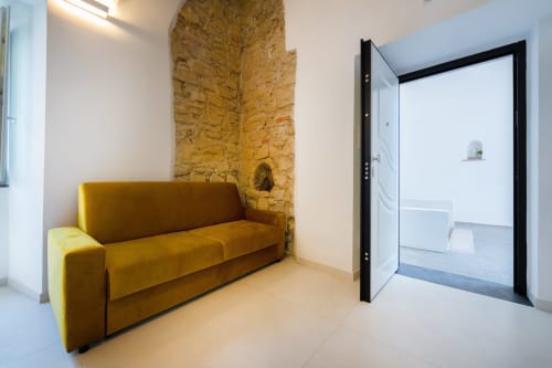 Ingresso moderno di Origenes Rooms Procida con divano senape, muro in pietra a vista e porta d'ingresso in vetro