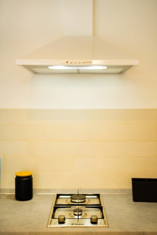Cucina moderna con piano cottura a gas, cappa aspirante e schienale color crema nell'appartamento Era di Origenes Rooms, Procida