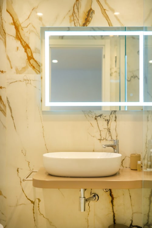 Bagno moderno presso Origenes Rooms, Procida con pareti in marmo, lavabo bianco a bacinella e specchio illuminato