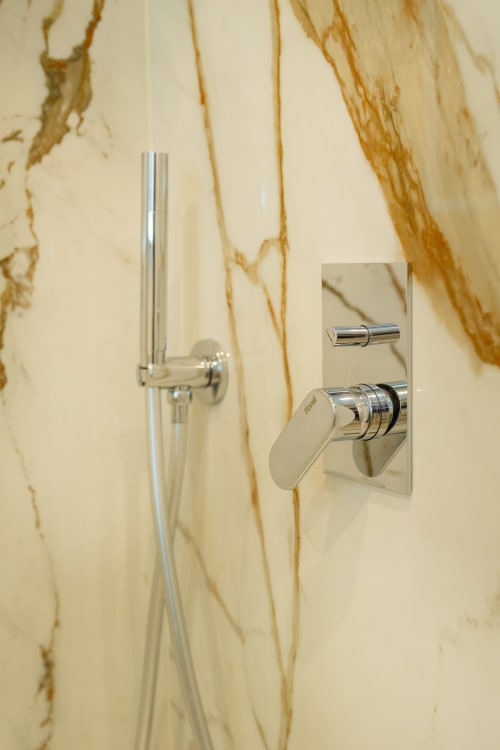 Moderni rubinetti doccia cromati su parete in marmo con venature dorate nell'appartamento Origenes Rooms, Procida