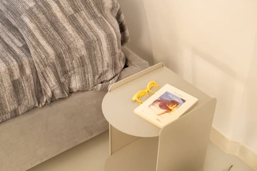 Occhiali da sole gialli e cartolina sul comodino bianco accanto al letto di Origenes Rooms, Procida