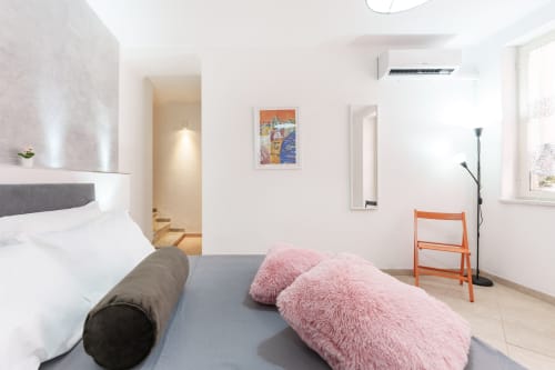 Modern bedroom at Origenes Rooms in Procida with double bed, pink cushions, orange chair, and minimalist decor