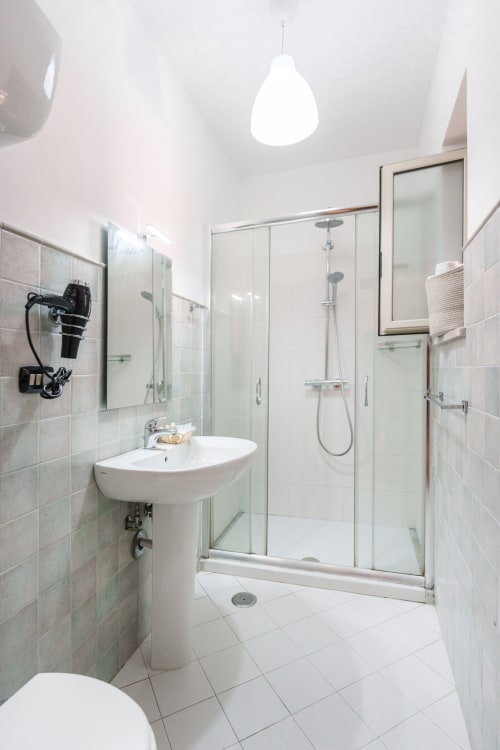 Modern bathroom at Origenes Rooms, Procida with pedestal sink, glass shower enclosure, and white tile flooring