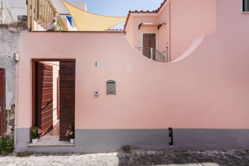 Pink and gray Mediterranean townhouse exterior with dark wooden door at Origenes Rooms, Procida, Italy