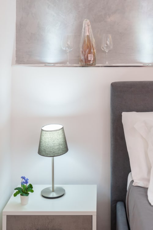 Elegant bedroom at Origenes Rooms, Procida with modern lamp, potted flowers, and champagne bottle display above gray