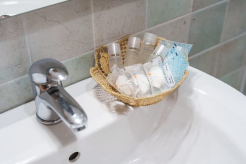Bathroom sink at Origenes Rooms with woven basket of complimentary toiletries, chrome faucet, and tiled backsplash