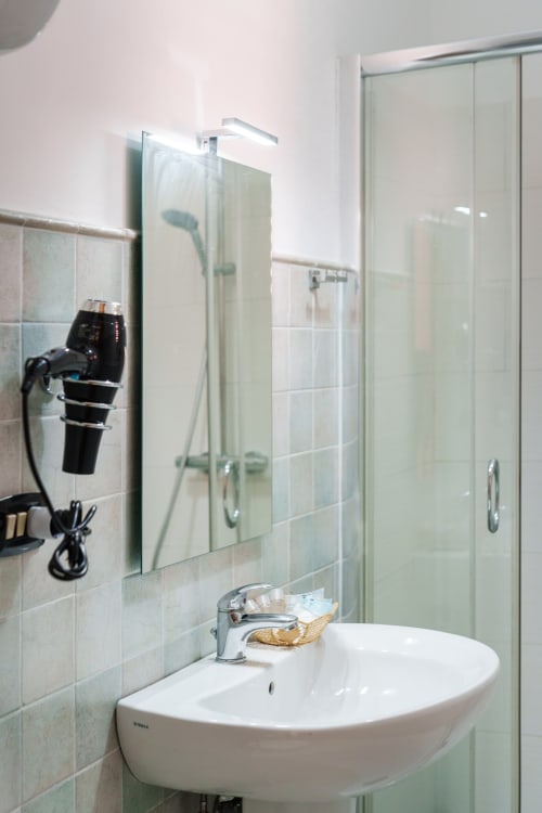 Modern bathroom at Origenes Rooms in Procida with white sink, tiled walls, glass shower enclosure, and bathroom amenities