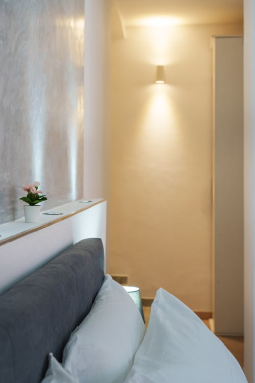 Modern bedroom at Origenes Rooms in Procida with white bedding, minimalist desk, potted flower, and warm ambient lighting